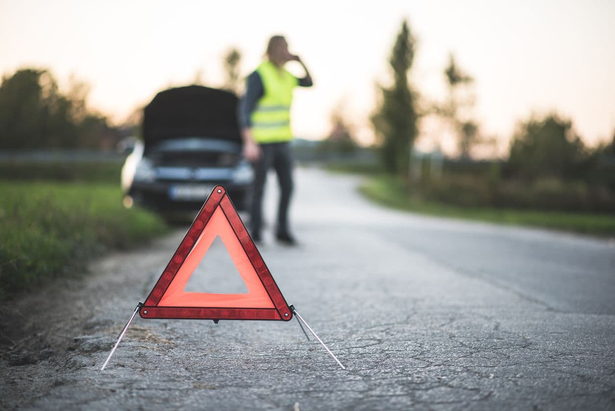 Un triangle de pré-signalisation installé en amont d'un véhicule en panne.